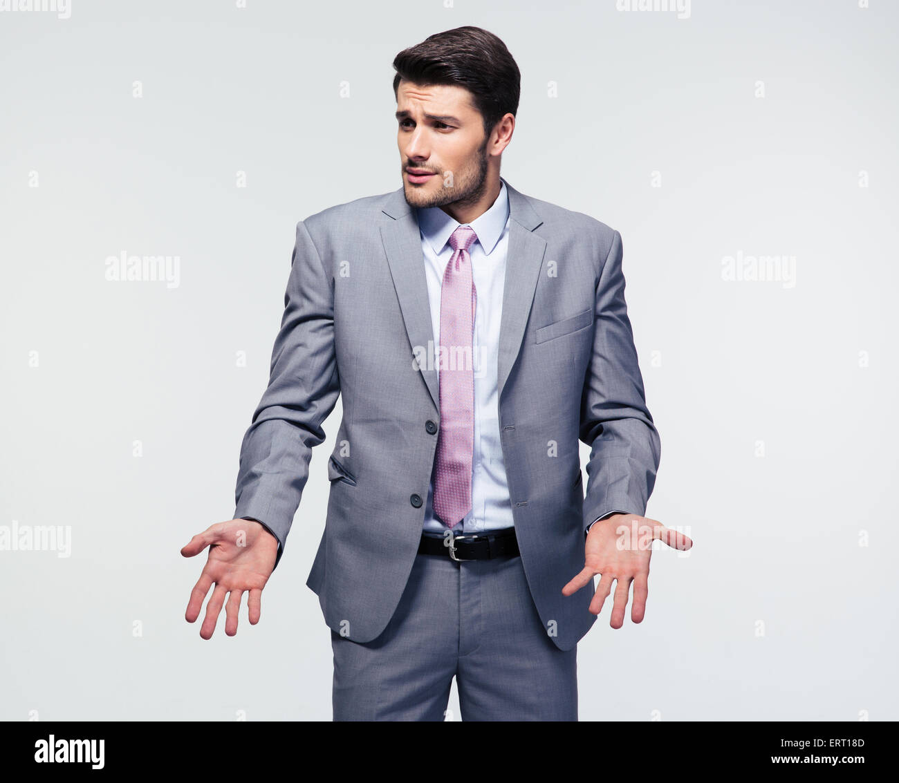Businessman shrugging shoulders over gray background. Looking at camera Stock Photo