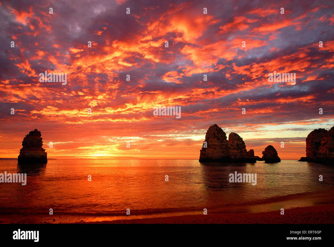 Stunning sunrise over the ocean with beautiful red clouds and a few cliffs standing out of the water Stock Photo