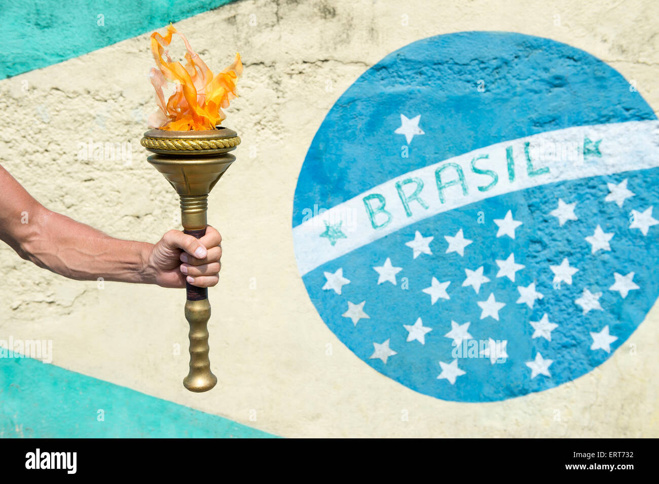 Hand of Brazilian athlete holding sport torch in front of a Brasil flag mural Rio de Janeiro Brazil Stock Photo