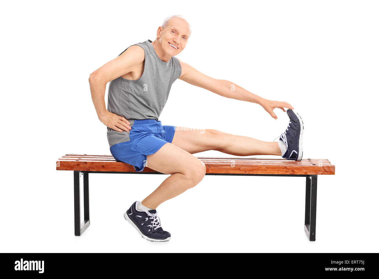 Senior in sportswear sitting on a wooden bench and stretching his leg isolated on white background Stock Photo