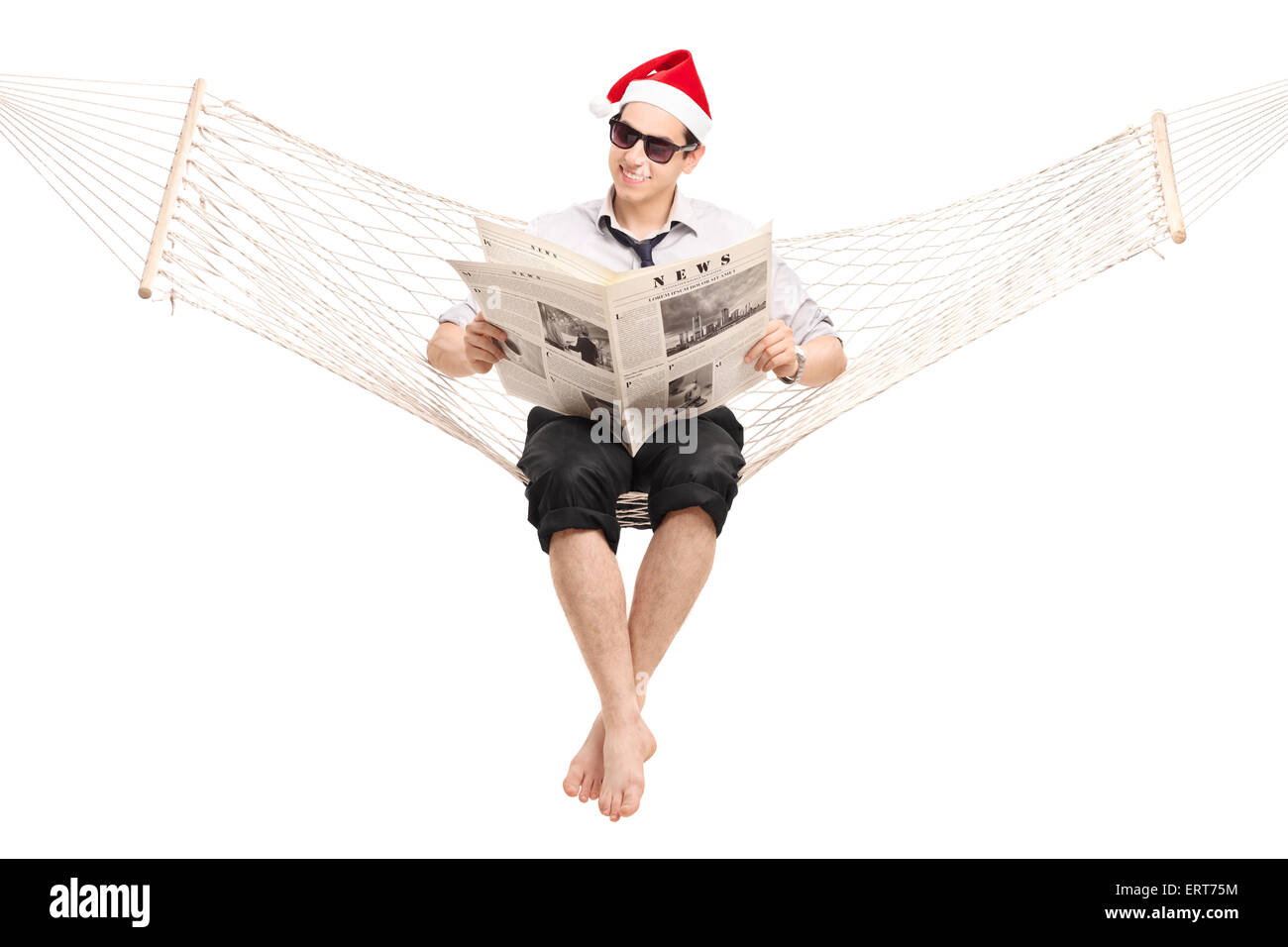 Young guy with Santa hat sitting in a hammock and reading a newspaper isolated on white background Stock Photo