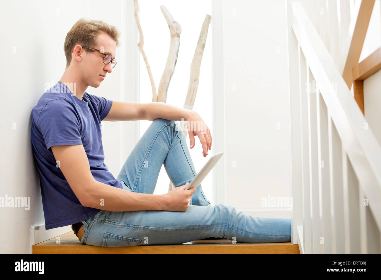 blond young man sitting on stairs with a tablet Stock Photo - Alamy