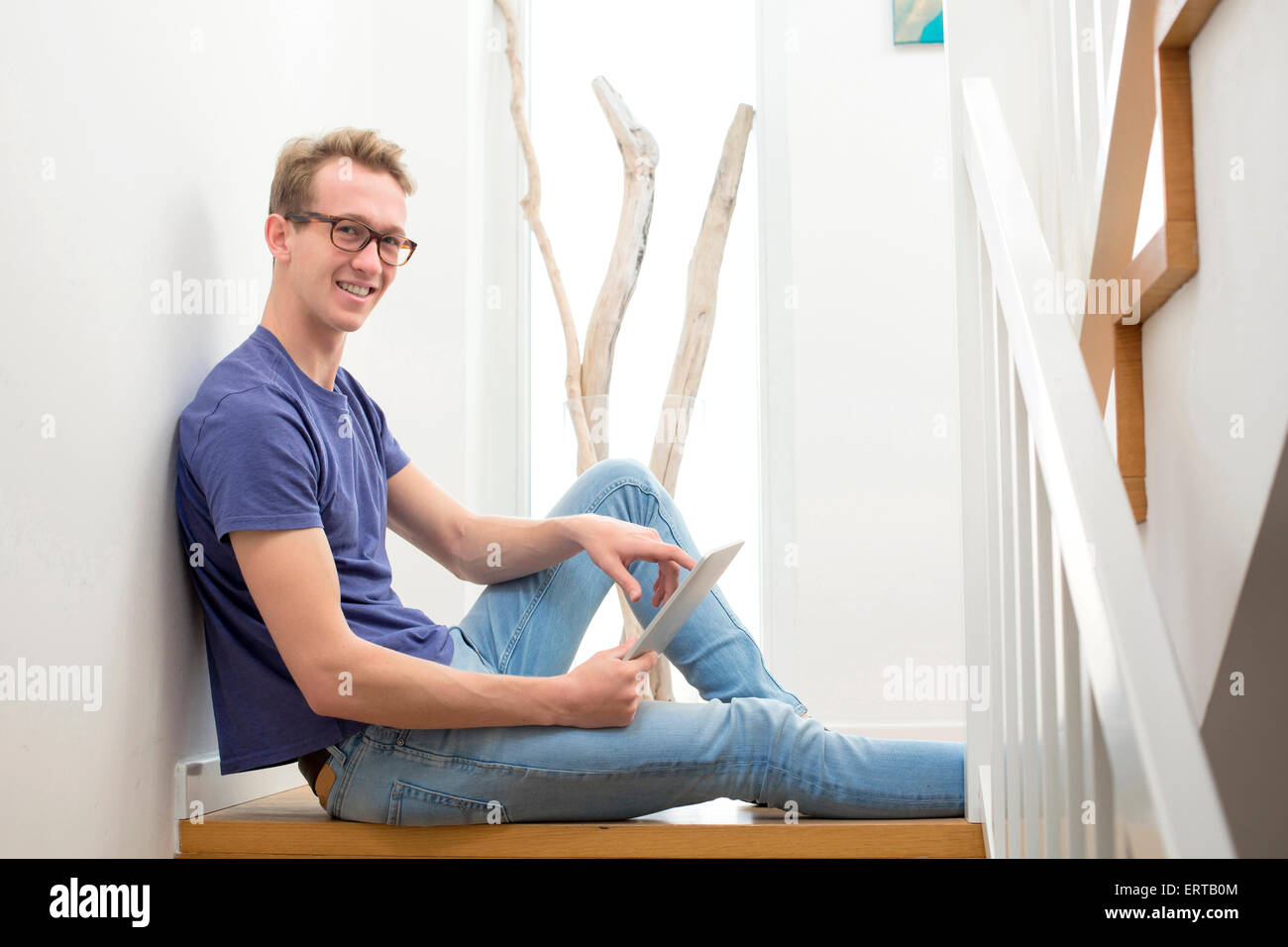 blond young man sitting on stairs with a tablet Stock Photo - Alamy