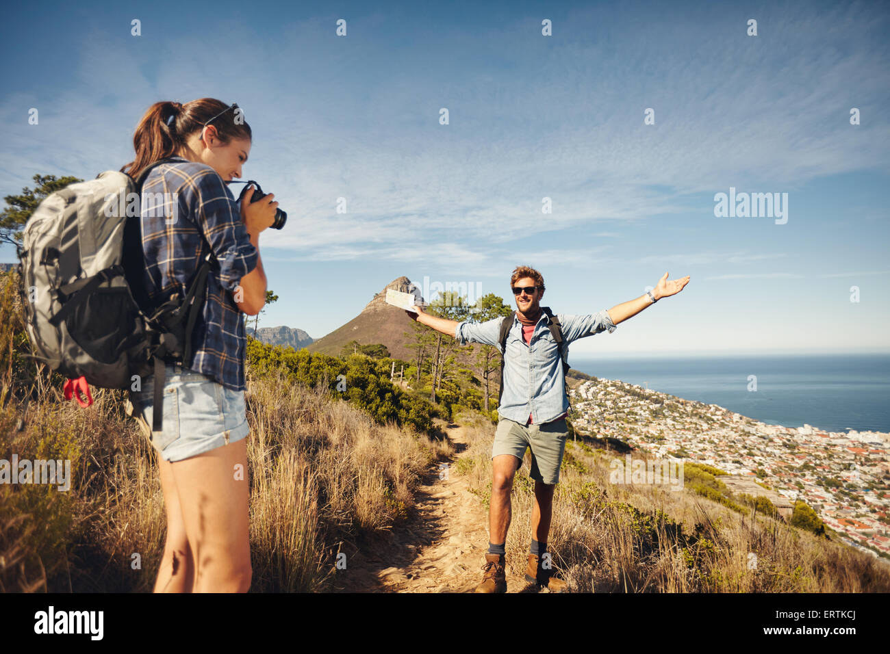Outdoor shot of young woman photographing her boyfriend in countryside while hiking. Hiker couple enjoying during summer vacatio Stock Photo