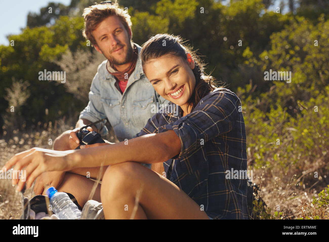Portrait of happy young woman with her boyfriend taking a break on a hike. Couple hiking on summer vacation, Woman looking at ca Stock Photo