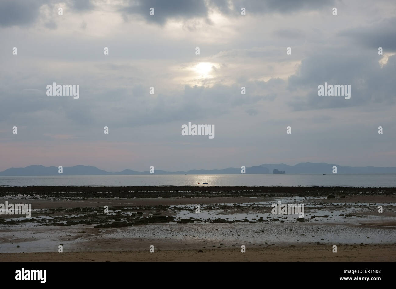 Sun setting behind clouds over Nong Thale Beach at low tide in Krabi Province, Thailand Stock Photo