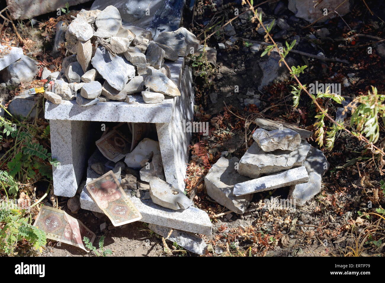 Small granite altar full of stones embedded in the ground of the mountain slope and showing some notes as money offerings. Tibet Stock Photo