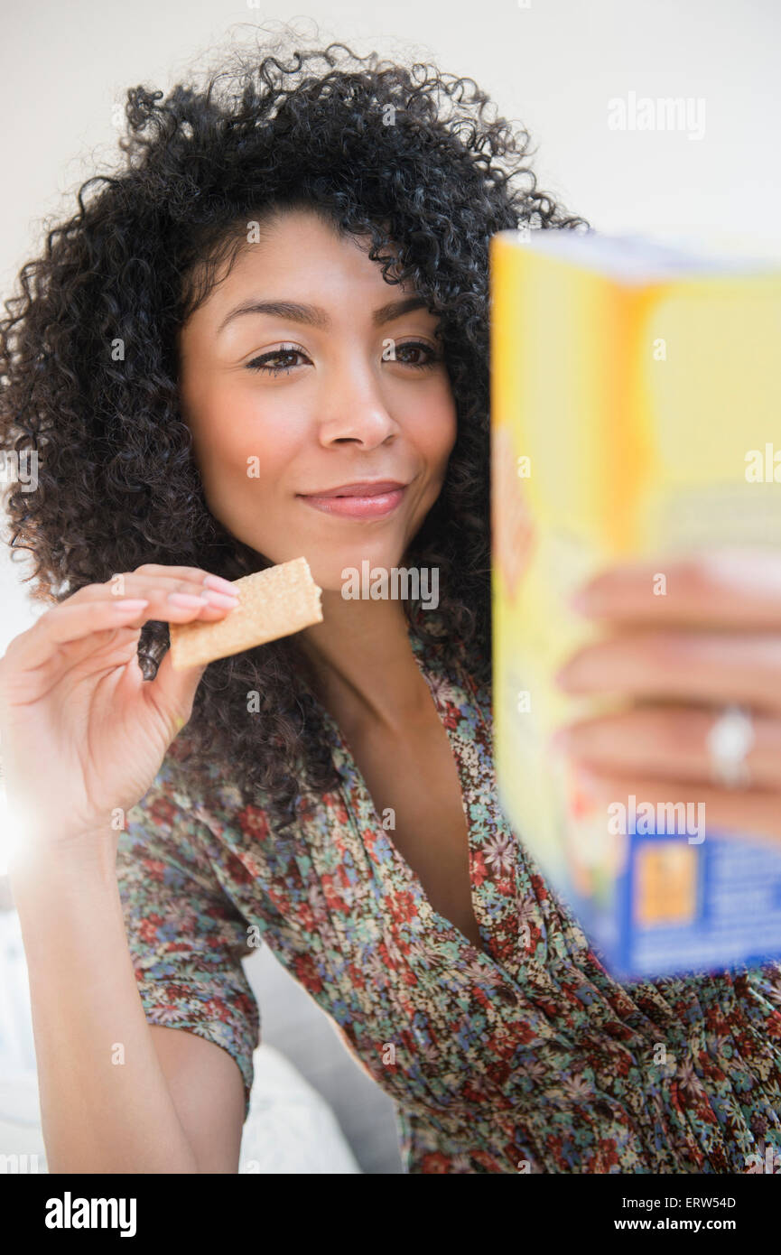 Mixed race woman eating cracker and reading nutrition information Stock Photo