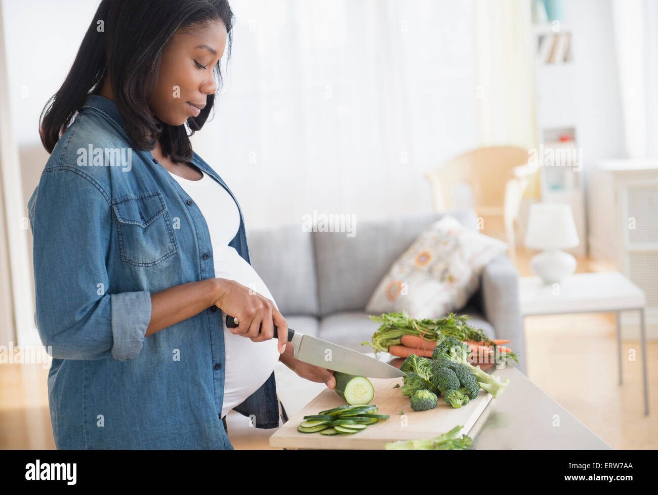 Black pregnant woman chopping vegetables in kitchen Stock Photo