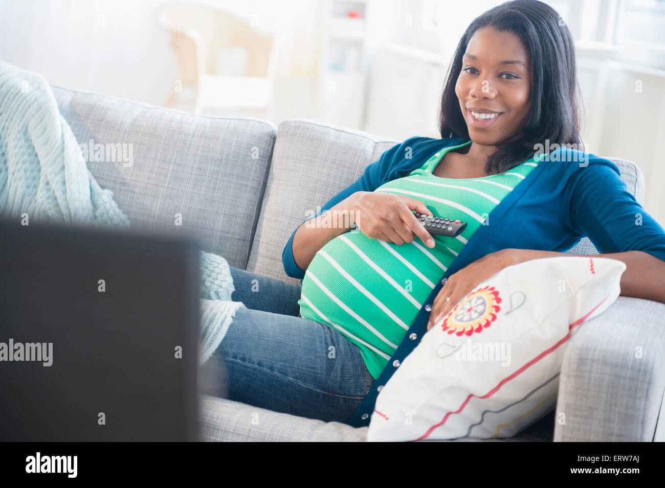 Black pregnant woman watching television on sofa Stock Photo