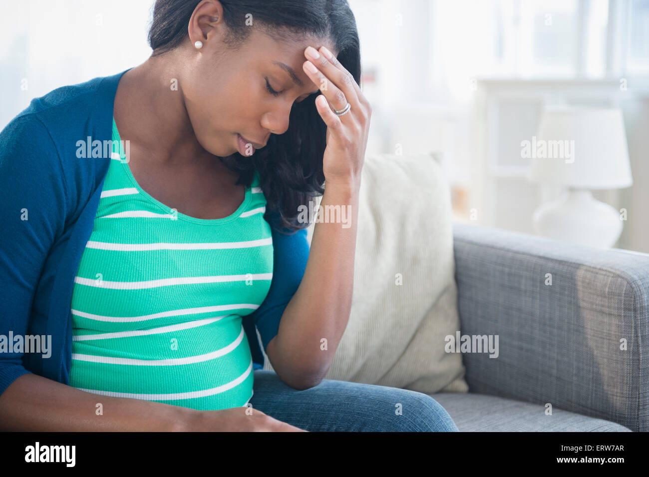 Anxious Black pregnant woman rubbing forehead on sofa Stock Photo