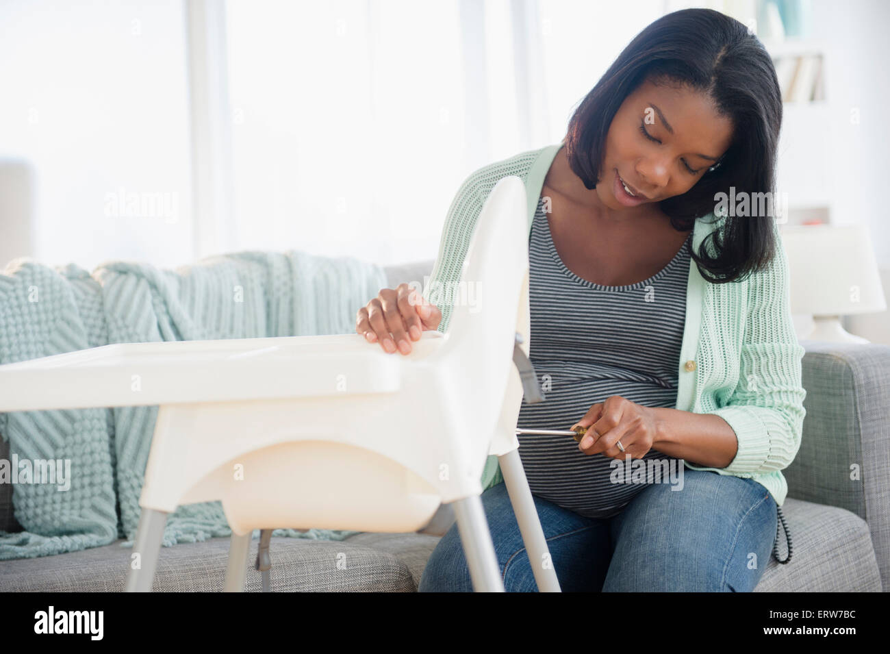 Black pregnant woman assembling high chair in living room Stock Photo