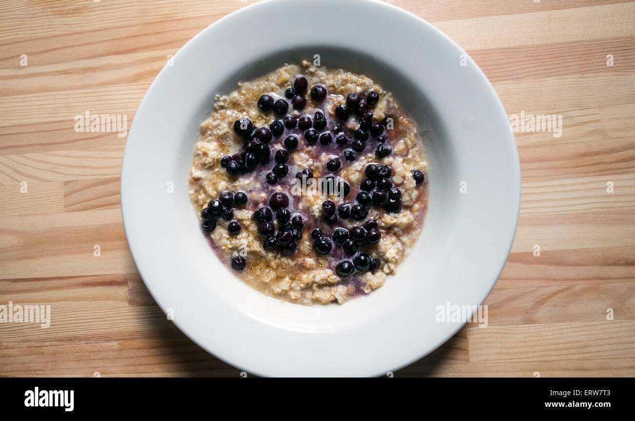 Oatmeal and small wild blueberries in a white bowl on a wooden table Stock Photo