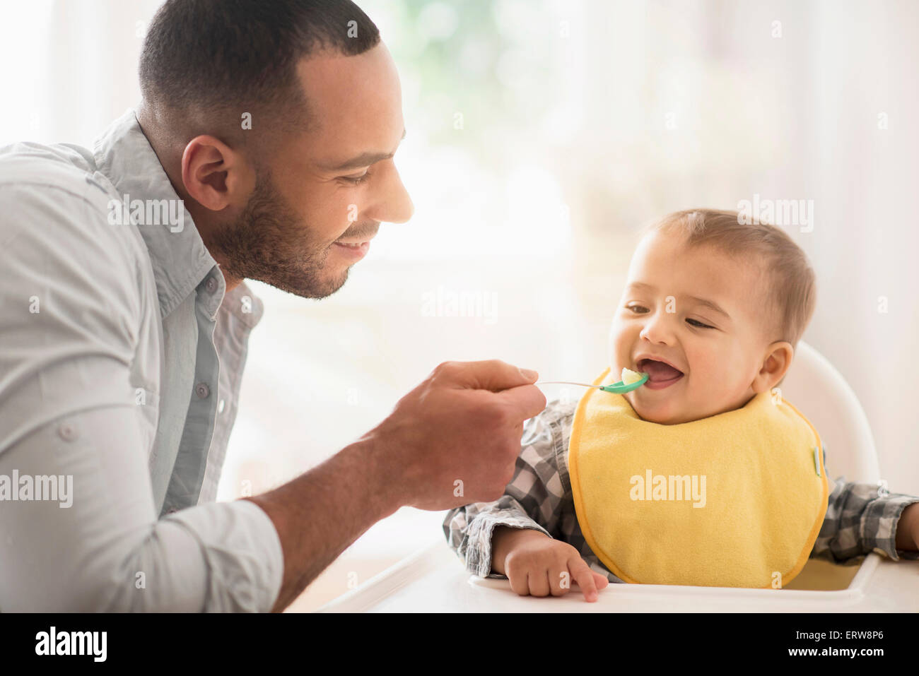 Father feeding baby son in high chair Stock Photo