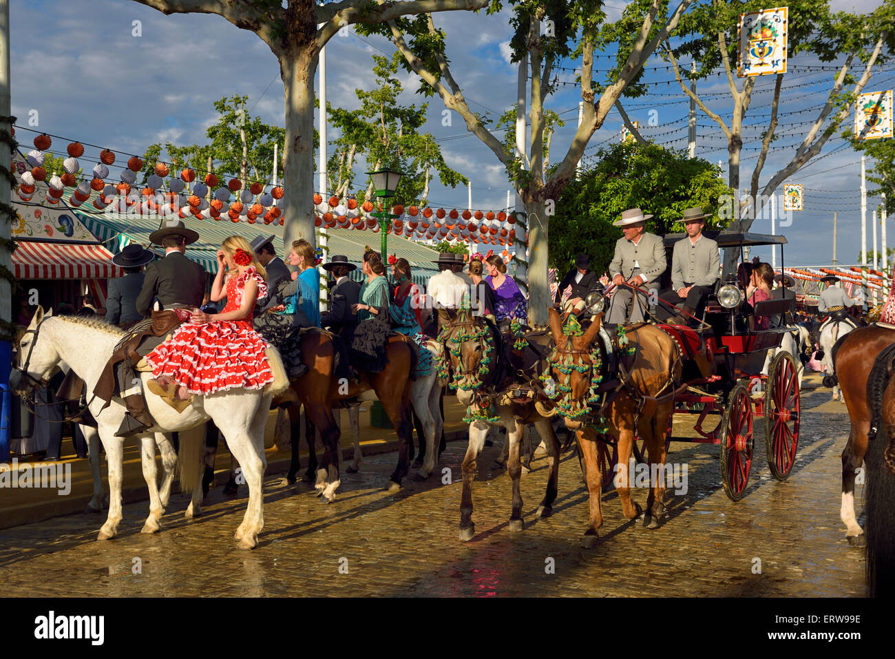 Couples on horseback and mules with carriage on cobblestone street at sunset Seville April Fair Spain Stock Photo