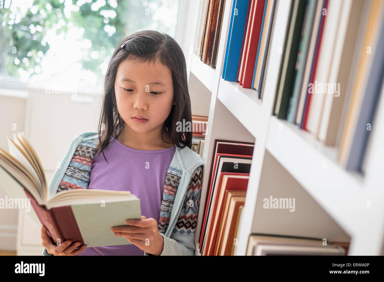 Chinese student reading book near library bookcase Stock Photo
