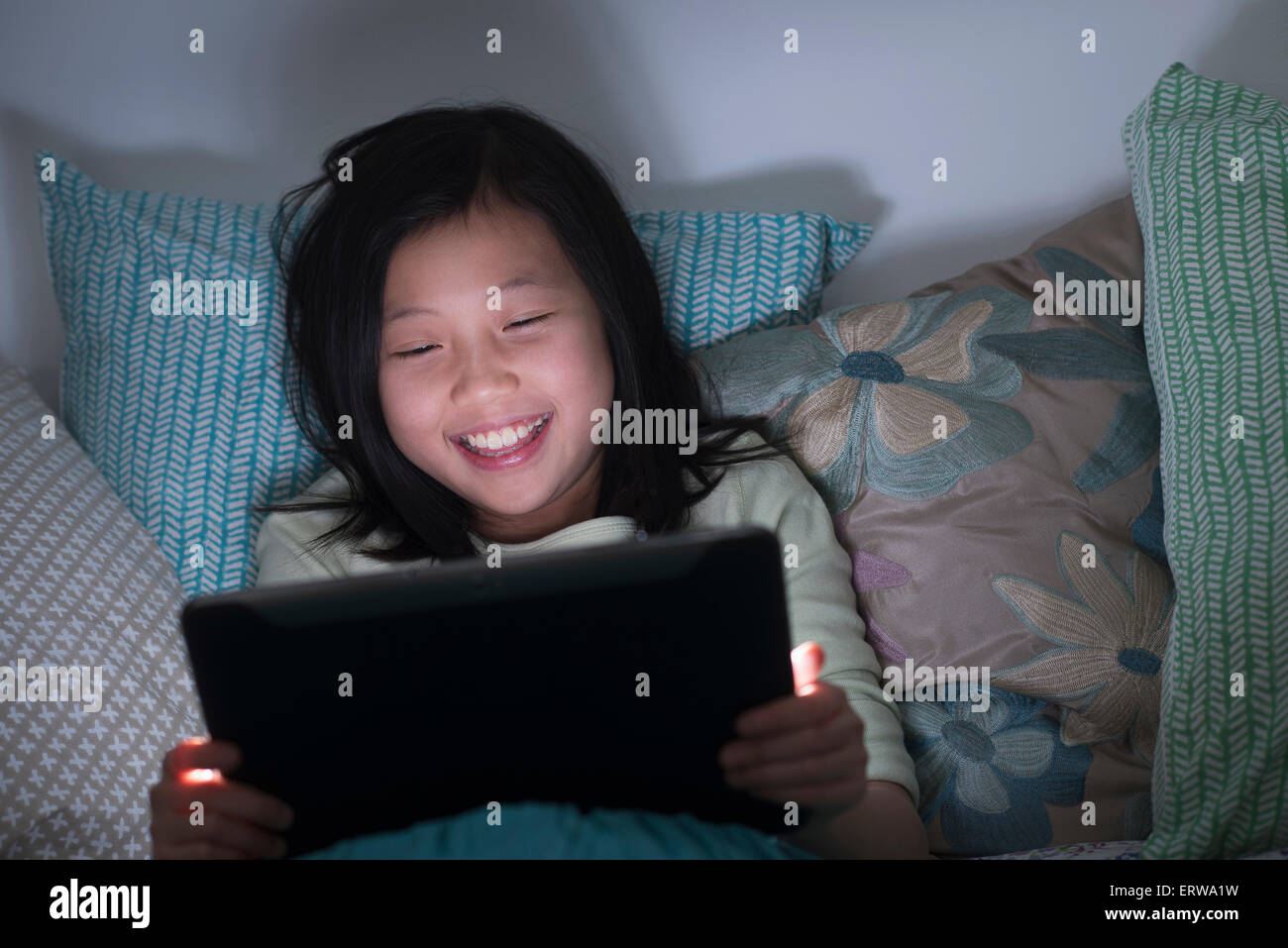 Smiling Chinese girl watching digital tablet in bed Stock Photo