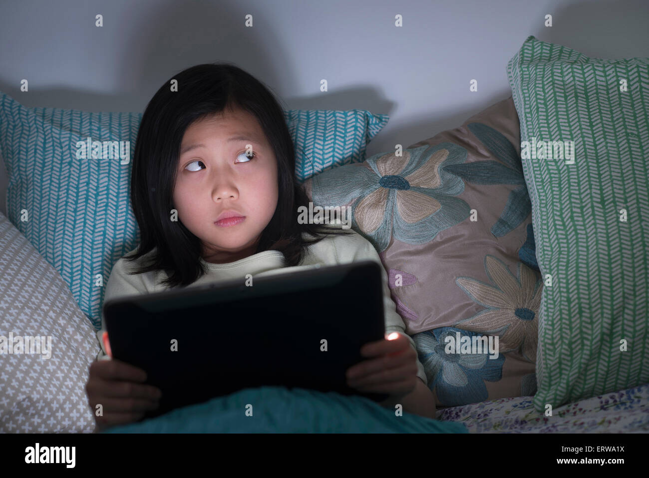 Nervous Chinese girl watching digital tablet in bed Stock Photo
