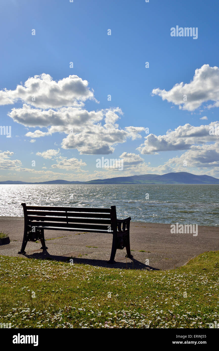 looking out into the solway coast on a bright sunny afternoon with a seat in the foreground blue sky and white fluffy clouds Stock Photo