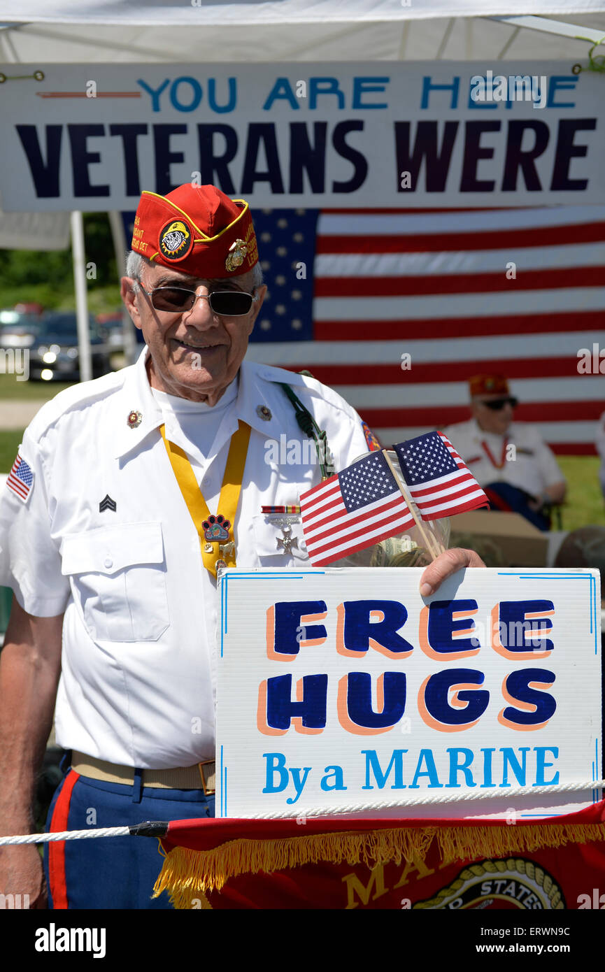 Old Westbury, New York. United States. 7th June 2015. Veteran JOHN GIORDANO, of Whitestone, holds a FREE HUGS By a MARINE sign at the fundraising booth of the Marine Corps League North Shore Queens Detachment #240 at the 50th Annual Spring Meet Car Show sponsored by Greater New York Region Antique Automobile Club of America. Over 1,000 antique, classic, and custom cars participated at the popular Long Island vintage car show held at historic Old Westbury Gardens. Stock Photo