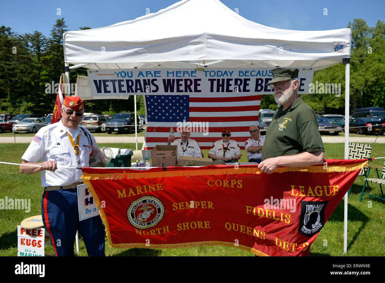 Old Westbury, New York, United States. 7th June 2015. JOHN GIORDANO of Whitestone, at left, and a fellow Marine veteran, hold a red Marine Corps League banner, in front of FREE HUGS By a MARINE fundraising booth of the Marine Corps League North Shore Queens Detachment #240 at the 50th Annual Spring Meet Car Show sponsored by Greater New York Region Antique Automobile Club of America. Over 1,000 antique, classic, and custom cars participated at the popular Long Island vintage car show held at historic Old Westbury Gardens. Stock Photo