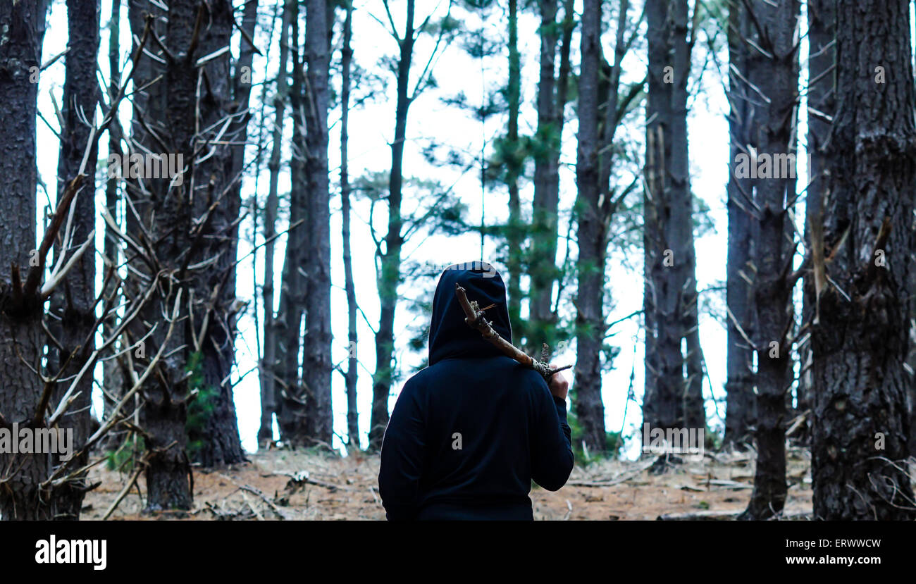 Hooded person in the woods with stick sword. Stock Photo