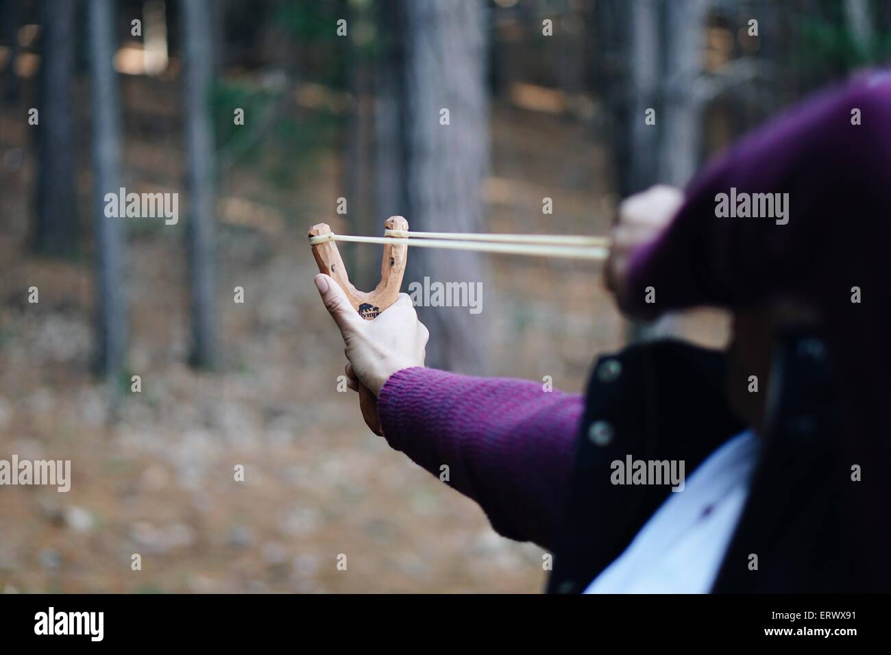 Woman aiming and shooting with a slingshot in the forest. Stock Photo