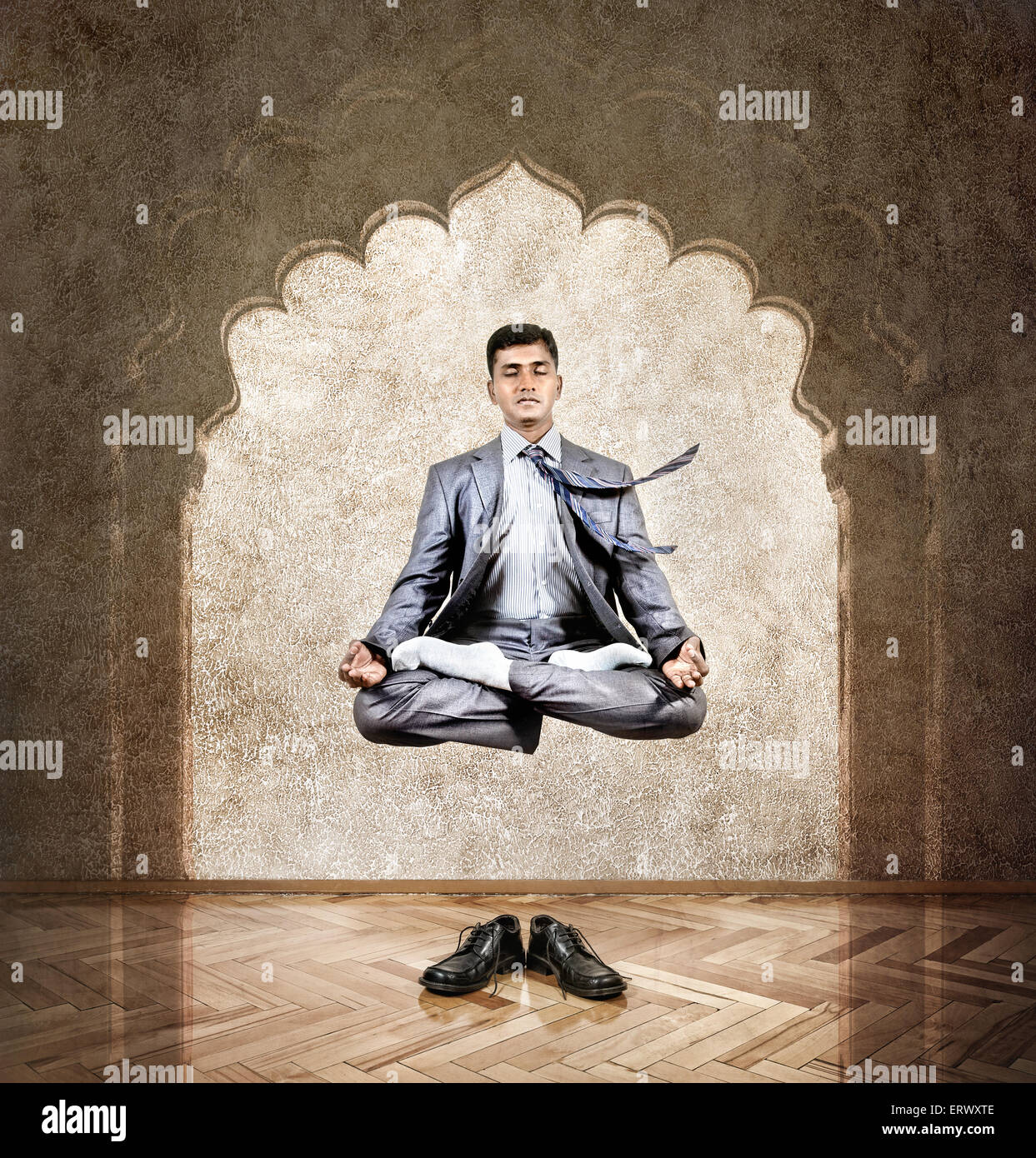 Indian businessman doing meditation in the air in lotus pose at the office with arch on the wall Stock Photo