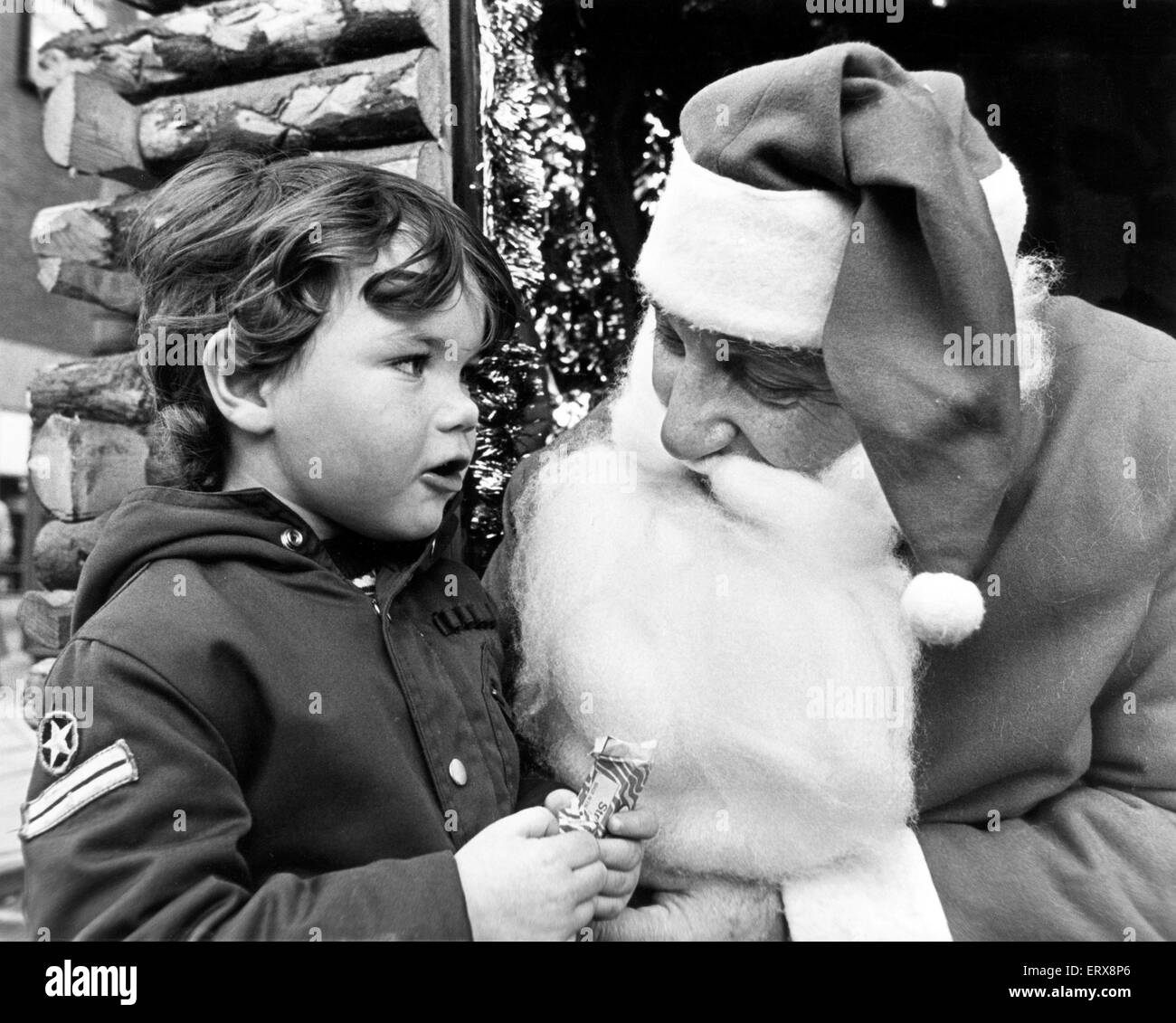 Three year old Matthew whispers his Christmas wishes to Father Christmas, who is on municipal duty in his log cabin in John Walker Square, Stockton. 18th December 1980. Stock Photo