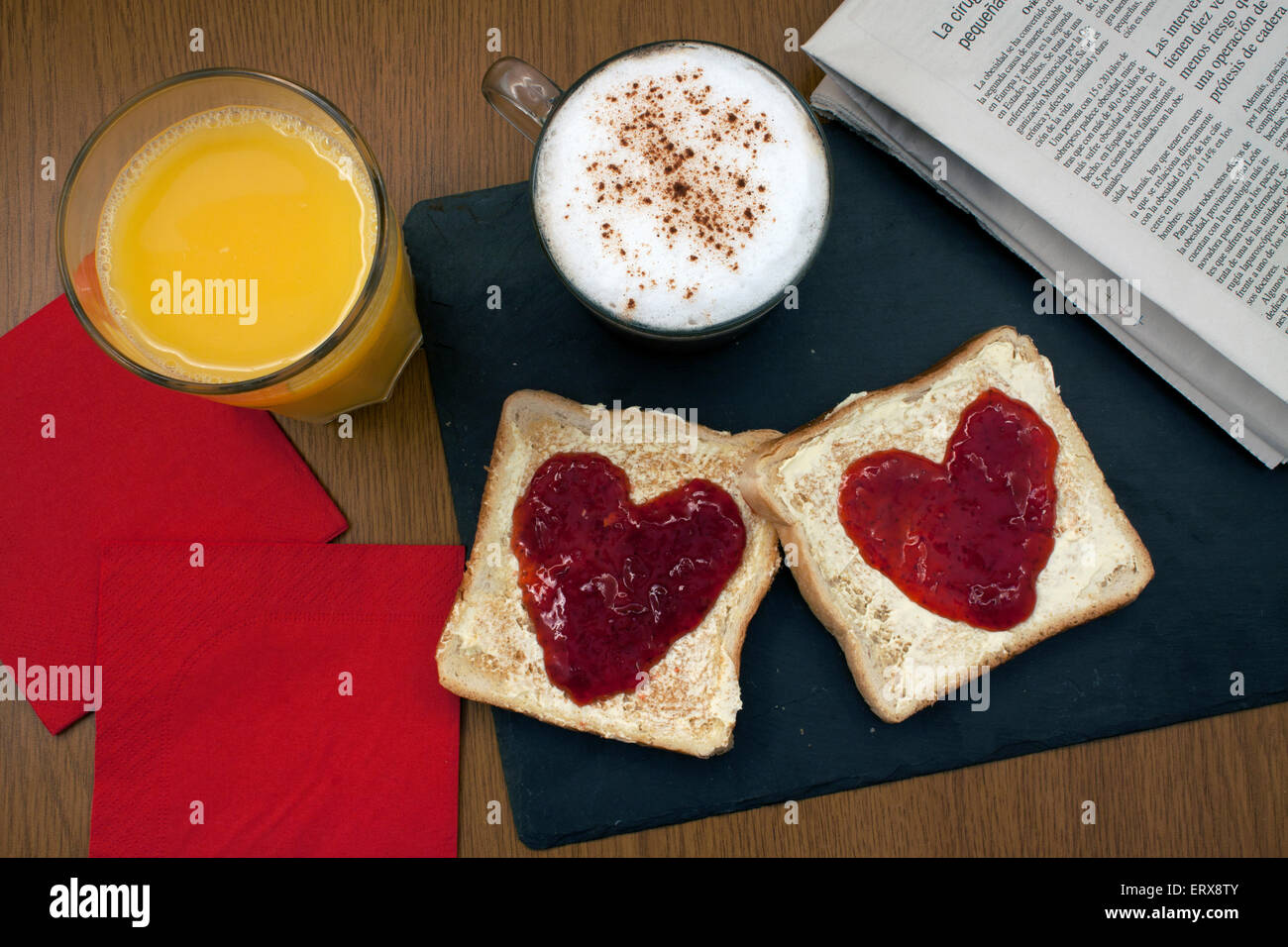 a prepared romantic breakfast with toast with butter and jam in a heart shape and a coffee  nexto to a newpaper and a napkin Stock Photo