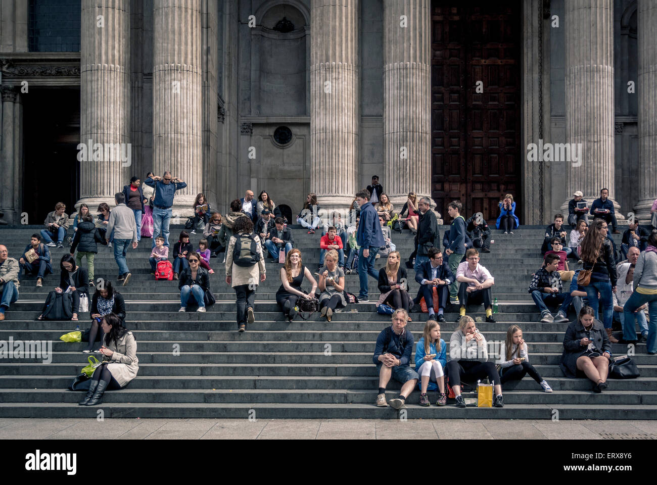 Tourists taking a break sitting on steps outside St Paul's Cathedral, London, UK. Stock Photo