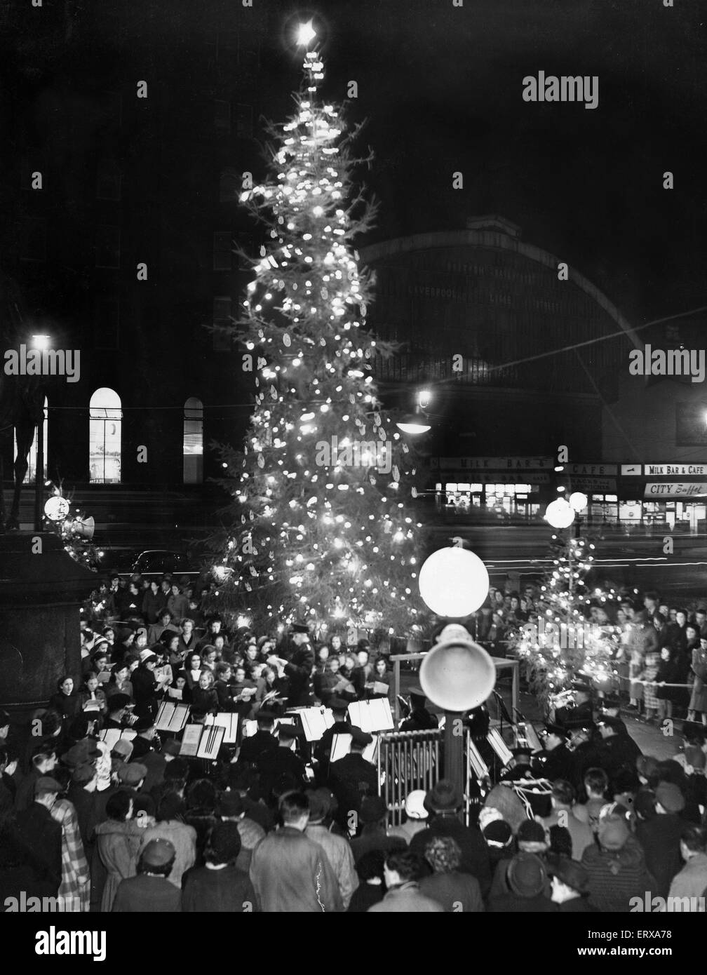 A Salvation Army band leads carol singers under magnificent tree in St George's plateau, opposite Lime Street, Liverpool. 20th December 1954 Stock Photo
