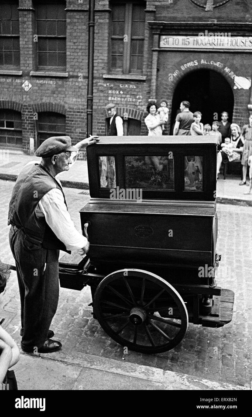 A man plays the barrel organ outside Hogarth Houses in Whitechapel, East London. Circa 1947. Stock Photo
