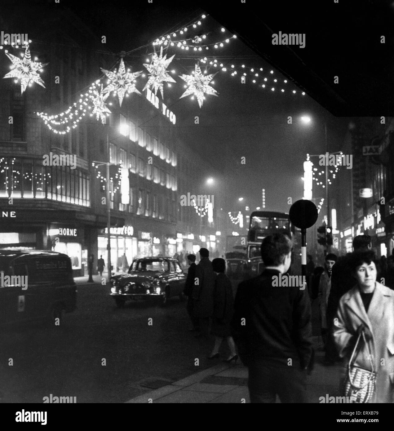 Christmas shopping as shimmering Stars hang over Lord Street in Liverpool, Merseyside, near the corner of Whitechapel and golden Christmas cracker suspended from lamp standards. 12th December 1962 Stock Photo