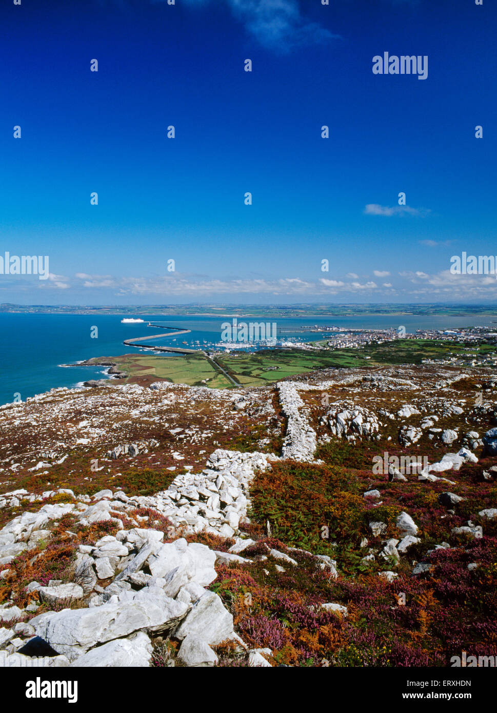 View along the ramparts of Caer y Twr Iron Age hillfort, Holyhead Mountain, Anglesey, to Holyhead harbour & breakwater, with departing Irish ferry. Stock Photo
