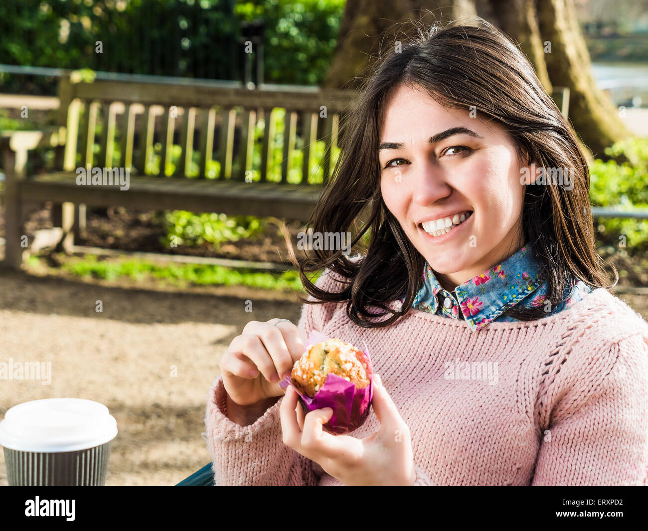 Beautiful Woman Having a Muffin Outside at the Coffee Shop and Looking at Camera with a Smile Stock Photo