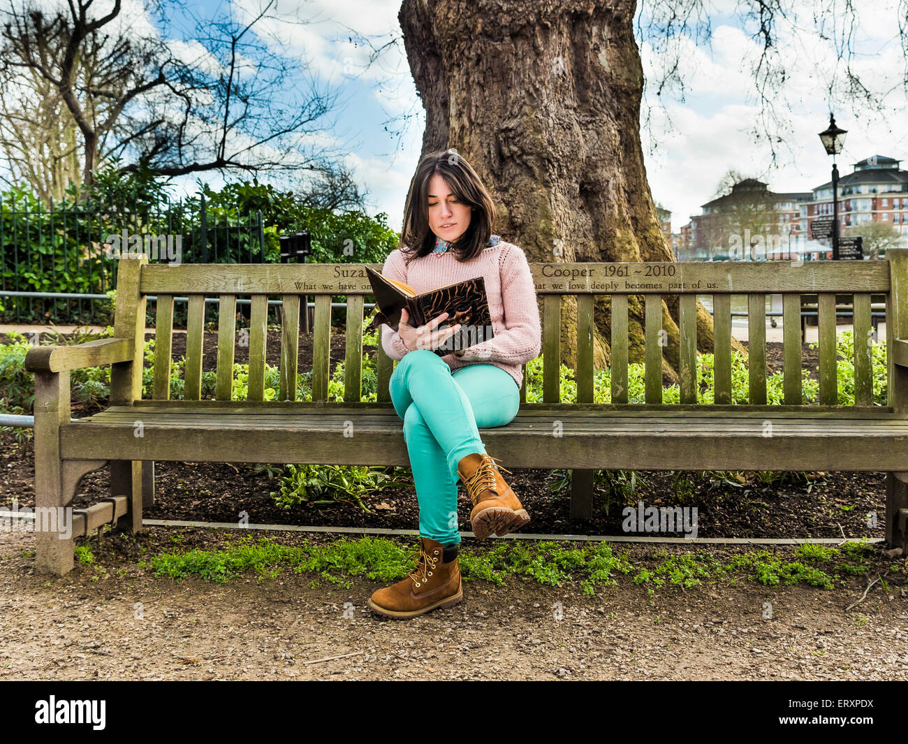 A Casual Young Woman Sitting on a Bench in a Park and Reading Her Book Stock Photo