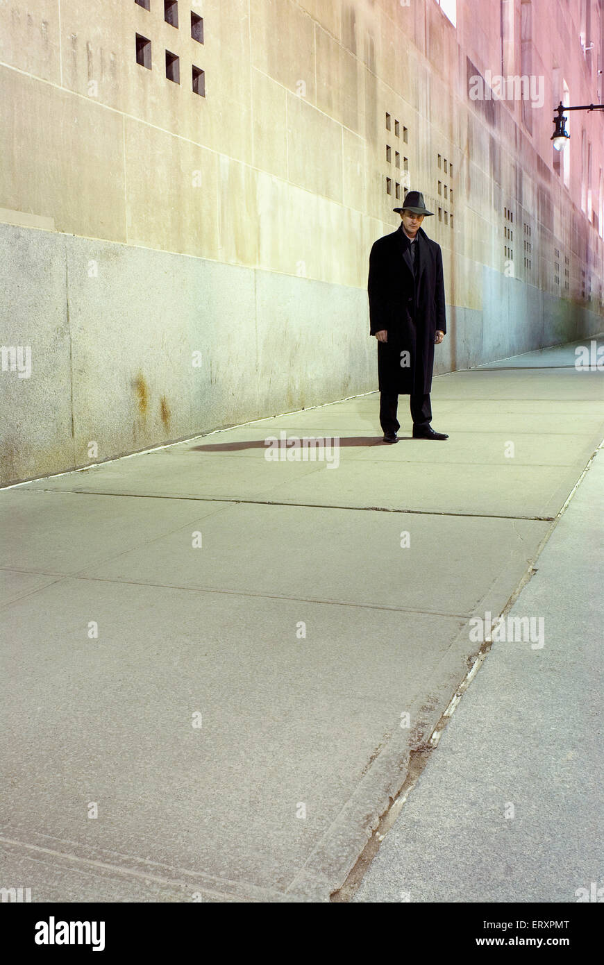 A man wearing a fedora hat standing mostly in shadow. Stock Photo