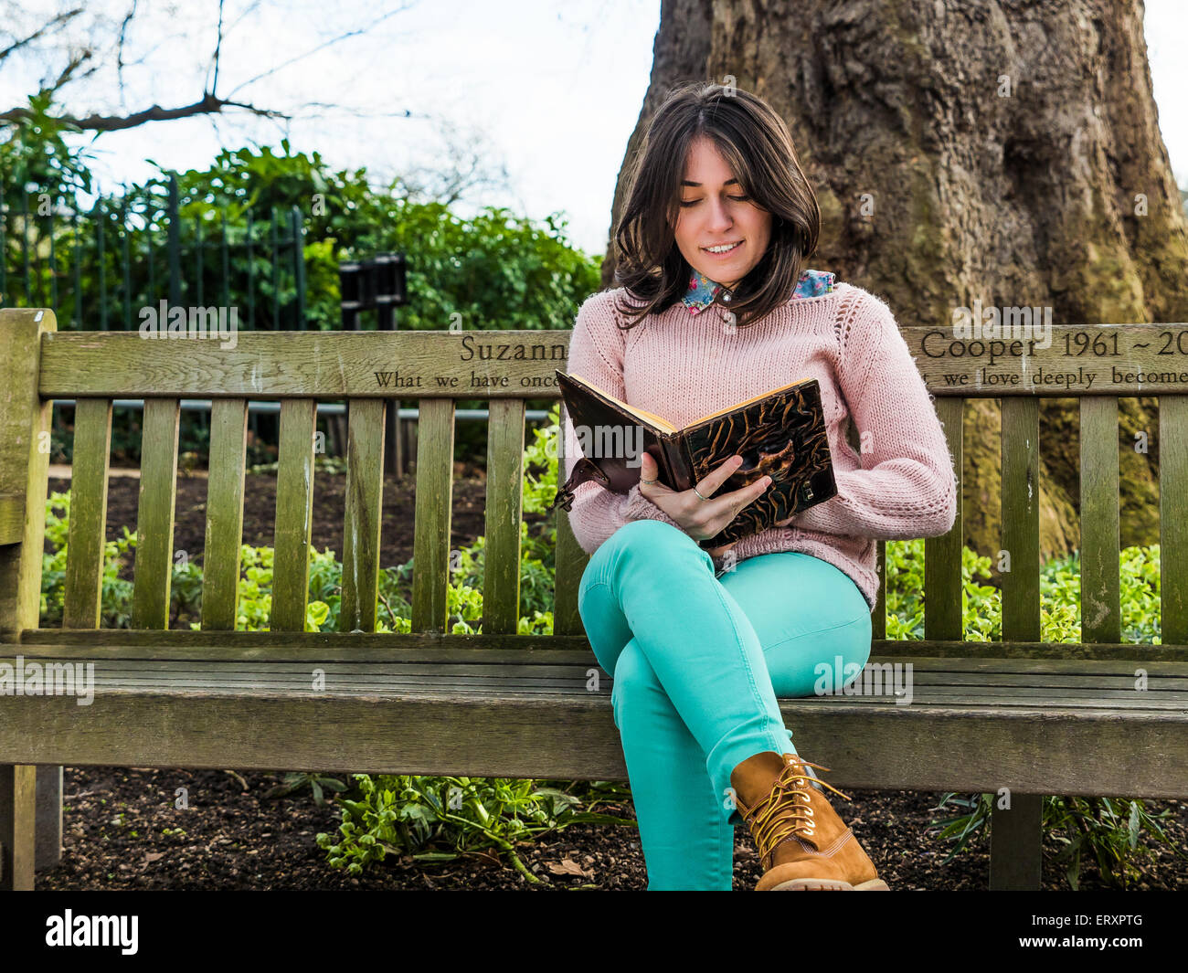 Pretty Woman Reading Book on Park Bench Stock Photo