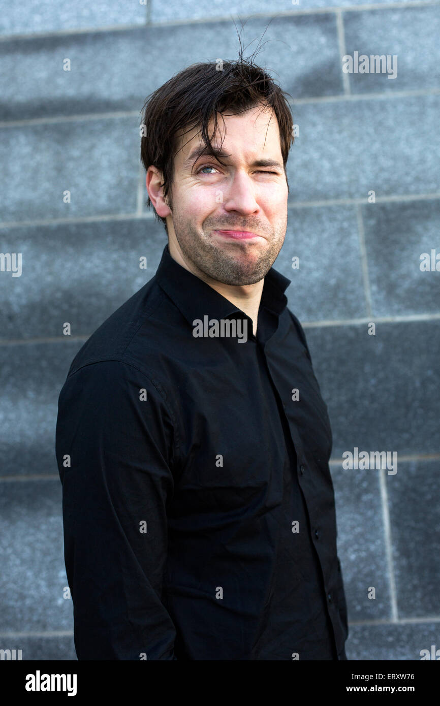 man in black shirt in front of wall is making faces Stock Photo