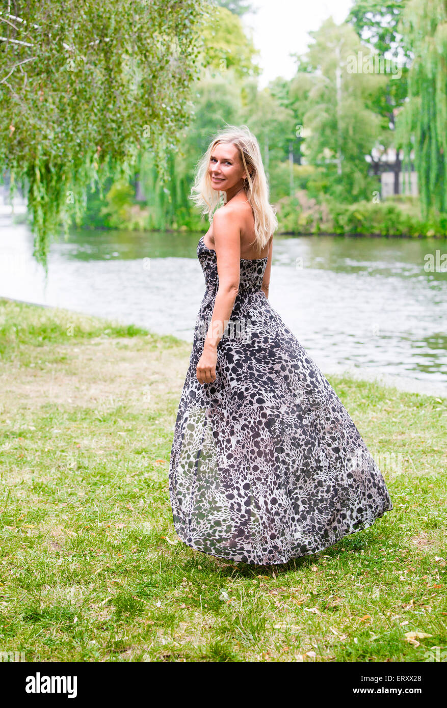 blond woman in a long dress standing by a river in a park Stock Photo ...