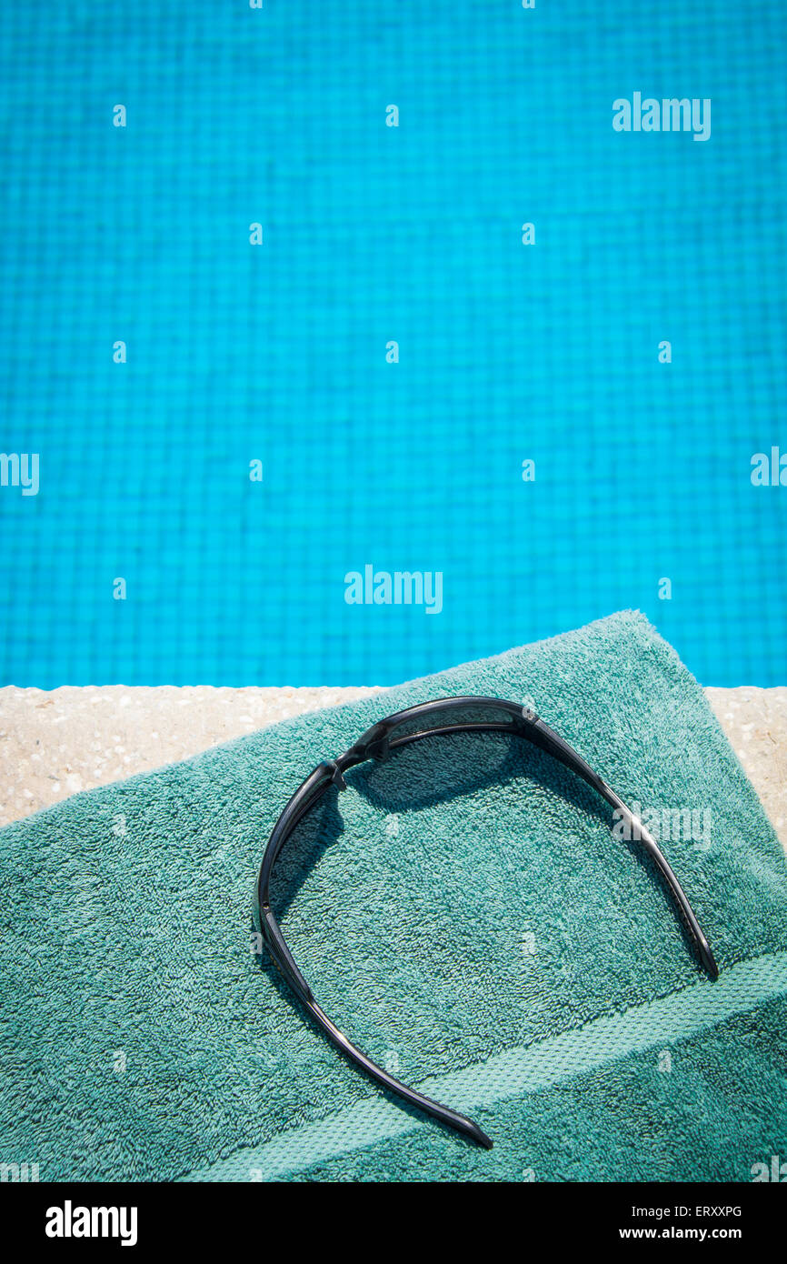Sunglasses and towel at the edge of swimming pool Stock Photo