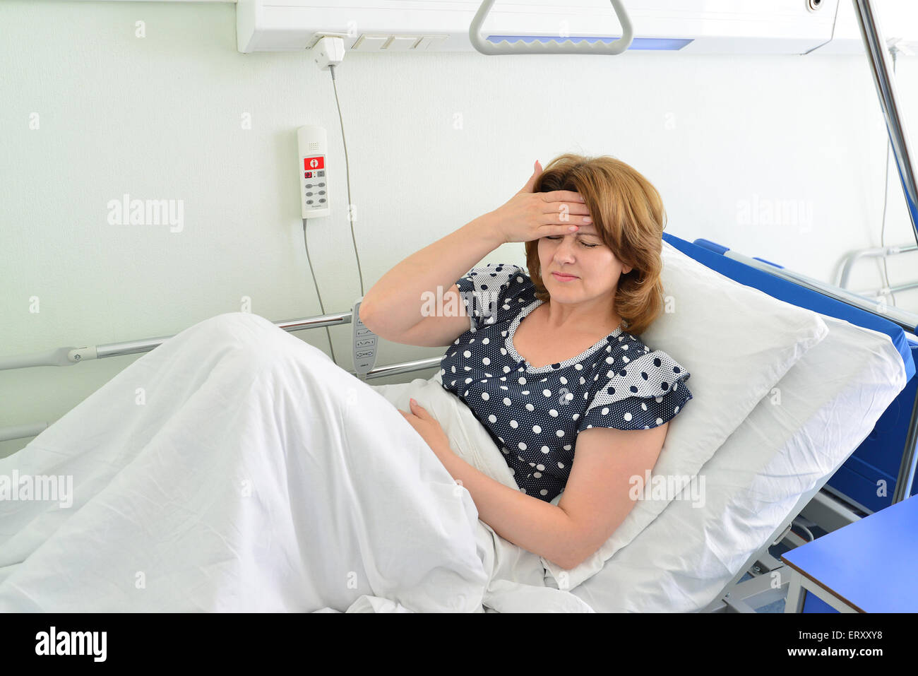 Female patient with headache on a bed in hospital ward Stock Photo
