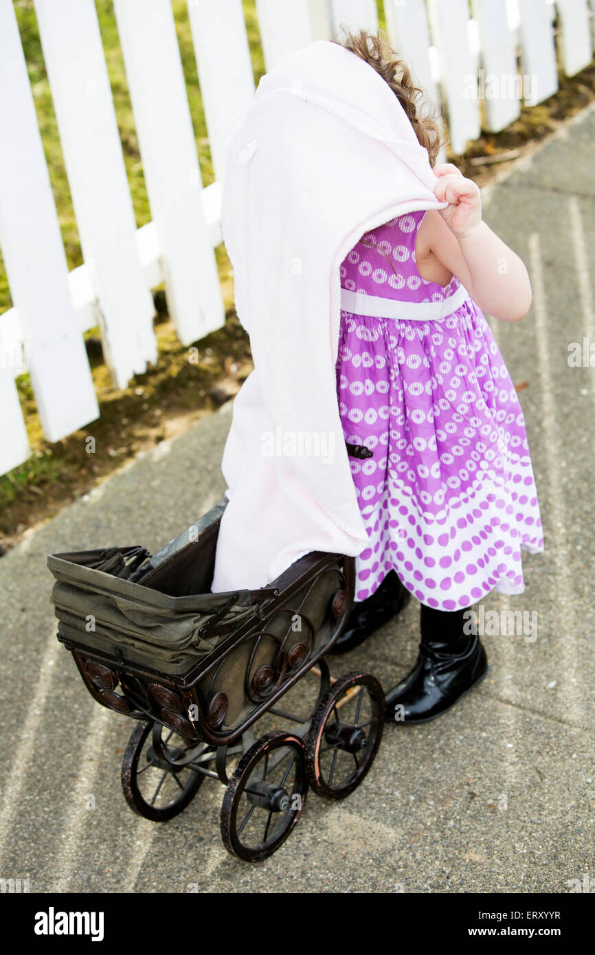 little girl in pink dress with her pram and blanket over head Stock