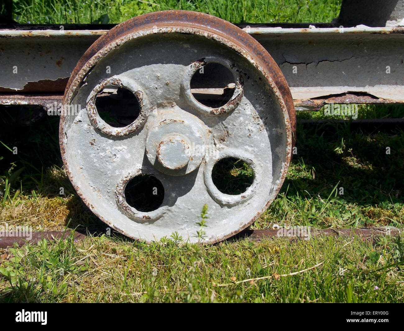 A contrast in textures - rust, flaking paint and grass as an old mine wagon rusts quietly in spring sunshine. Stock Photo
