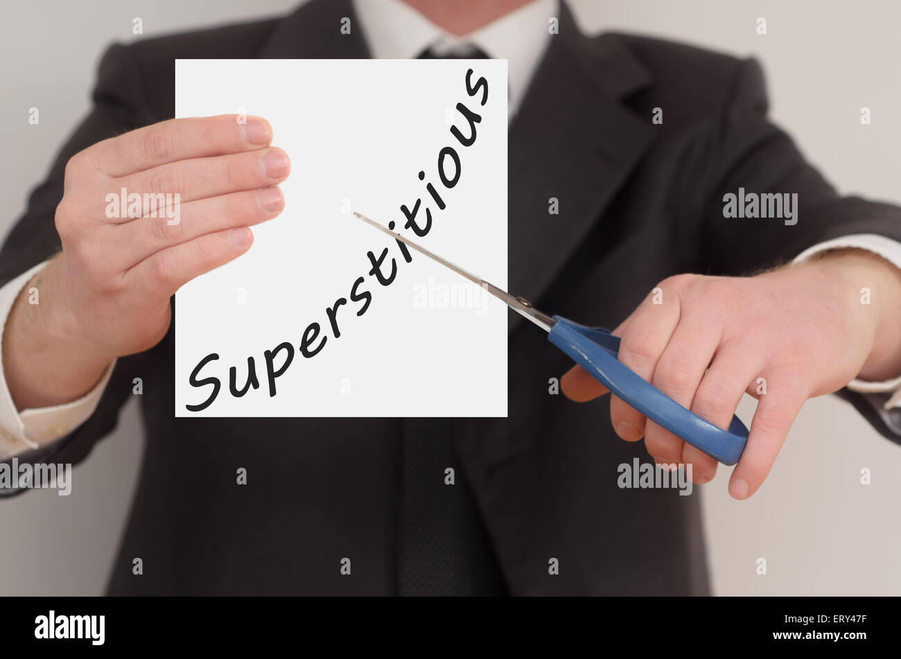 Superstitious, man in suit cutting text on paper with scissors Stock Photo