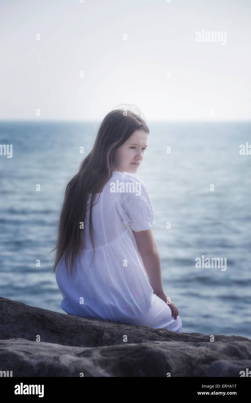 a girl in a white dress sitting on rocks at the sea Stock Photo