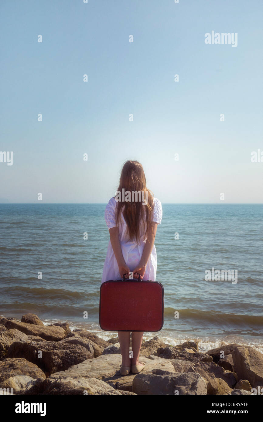 a girl with a red suitcase standing at the sea Stock Photo