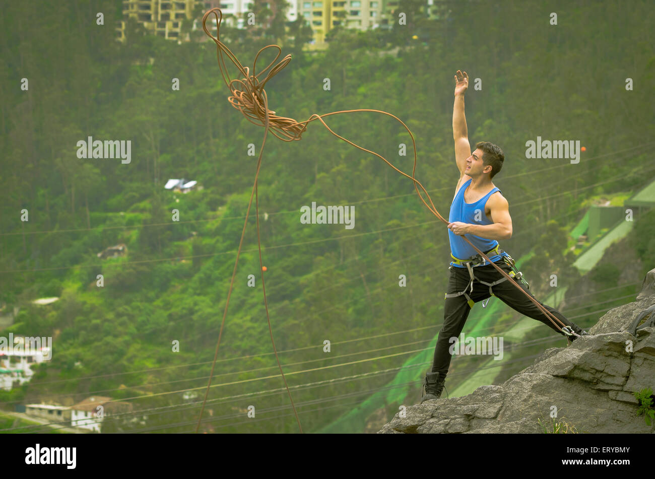 athletic man standing on cliff throwing rope down mountain Stock Photo