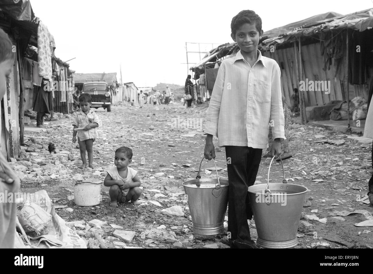 Boy carrying two buckets of water in Malvani slum ; Malad ; Bombay Mumbai ; Maharashtra ; India NO MR Stock Photo